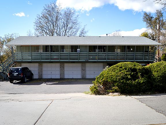 Front view of a multi-unit residential building with garages and a balcony, surrounded by greenery.