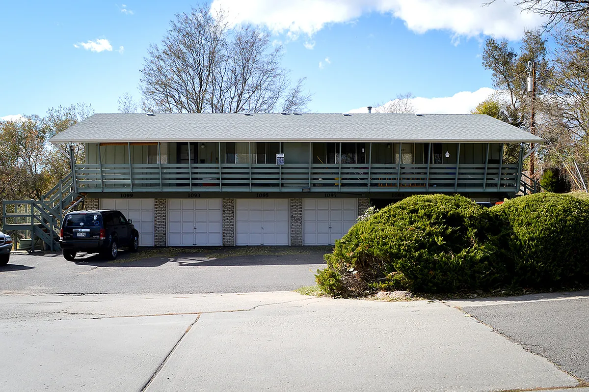 Front view of a multi-unit residential building with garages and a balcony, surrounded by greenery. - 1089 Lee St