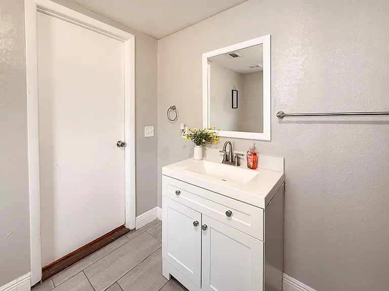 Bathroom vanity area with a single-sink cabinet, framed mirror, and towel bar, plus tile flooring for easy upkeep.
