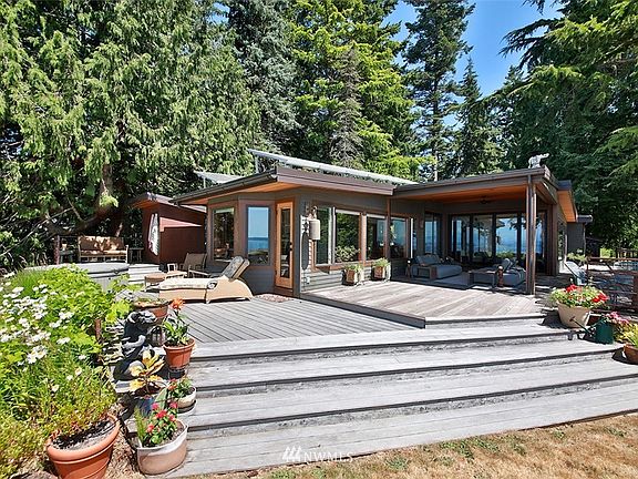Waterside of home with walls of windows & expansive wrap around Azek decking designed to provide ample space for entertaining while maximizing your unobstructed views. Notice the reflection of the water in the windows. 