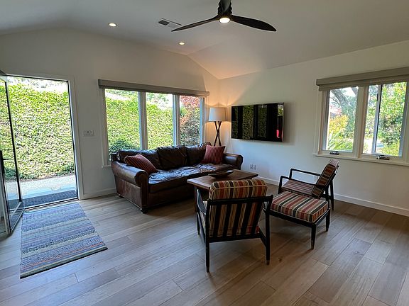 Light-filled living room with views to front yard and tenant's private garden. Furnished with large RH leather couch, coffee table, and TV. Hardwood floors throughout unit.