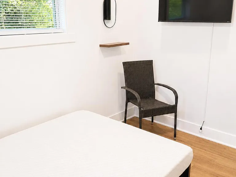 Private bedroom with a large window, wood-look flooring, and a wall-mounted TV plus a small sitting area.