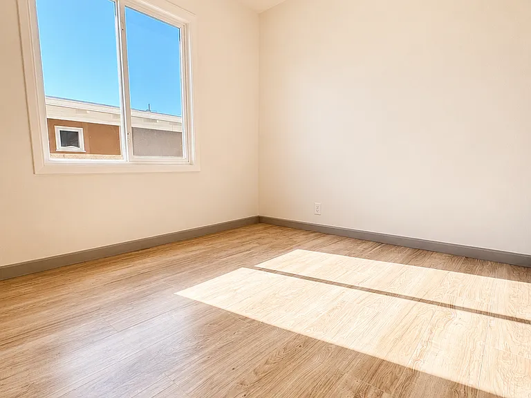 Sun-filled first bedroom with oversized window, warm wood-style flooring, and a clean modern finish _ bright, airy, and perfect for a peaceful retreat or productive work-from-home setup