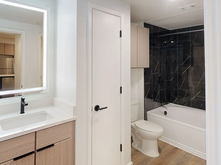 Apartment bathroom with wood-style flooring and LED vanity mirror.