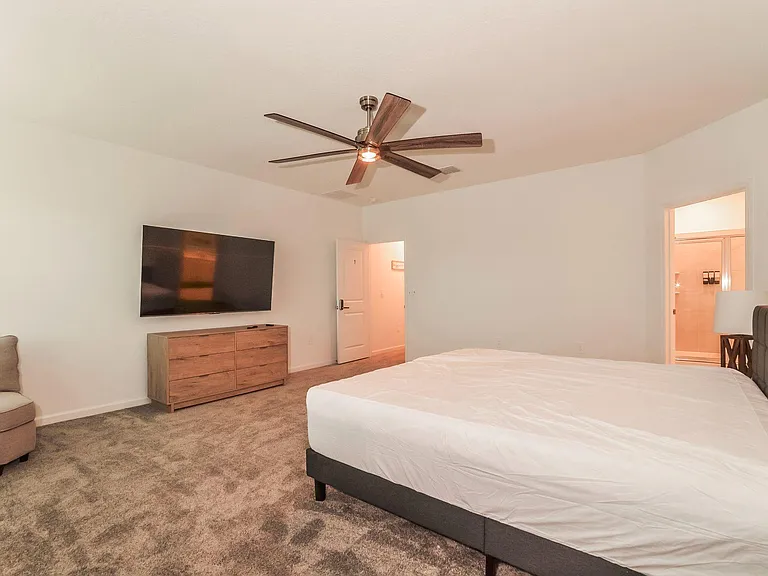 Spacious bedroom with a ceiling fan, wall-mounted TV, dresser storage, and private access to an en-suite bath.