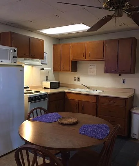 KITCHEN TABLE HAS FOUR CHAIRS AND IS LOCATED RIGHT UNDER A BIG CEILING FAN IN THE MIDDLE OF THE ROOM.