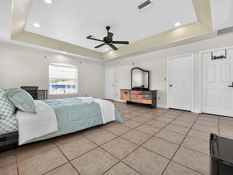 Spacious bedroom with tile flooring, ceiling fan, ample closet storage, and a desk area beside a large window.