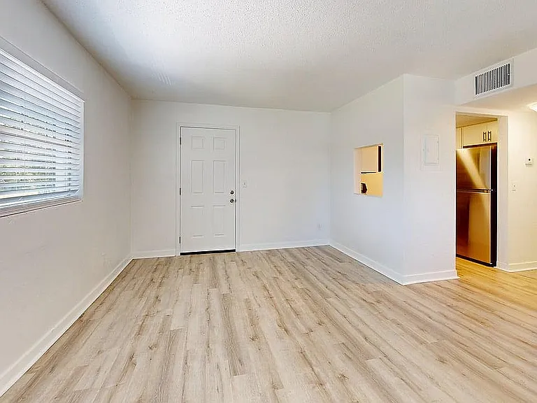 Bright and airy apartment with elegant wood flooring, large window with blinds, and modern stainless steel kitchen appliances.