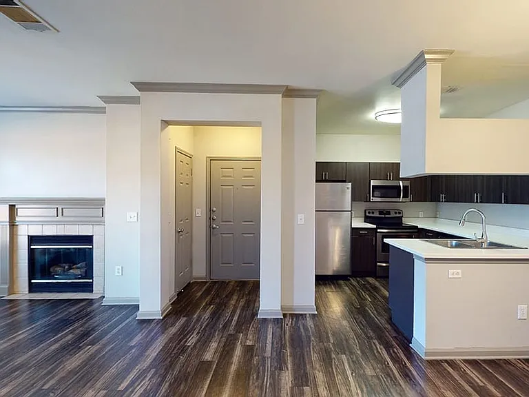 Apartment kitchen with stainless steel appliances, dining and living room with wood-style flooring.