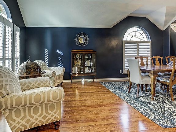 Greet your guests in the formal living room with immaculate wood floors, rich decorator paint, a raised ceiling with thick crown molding, and large windows with plantation shutters.