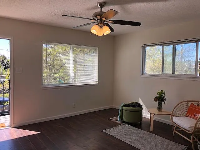Enter into the living space with wood laminate flooring, ceiling fan, large dual pane windows and a wall air conditioning unit.