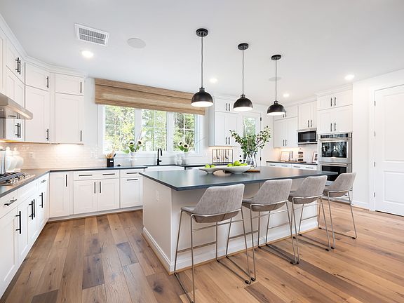 A modern, bright, and spacious kitchen with white cabinets, a large island with bar stools, and pend