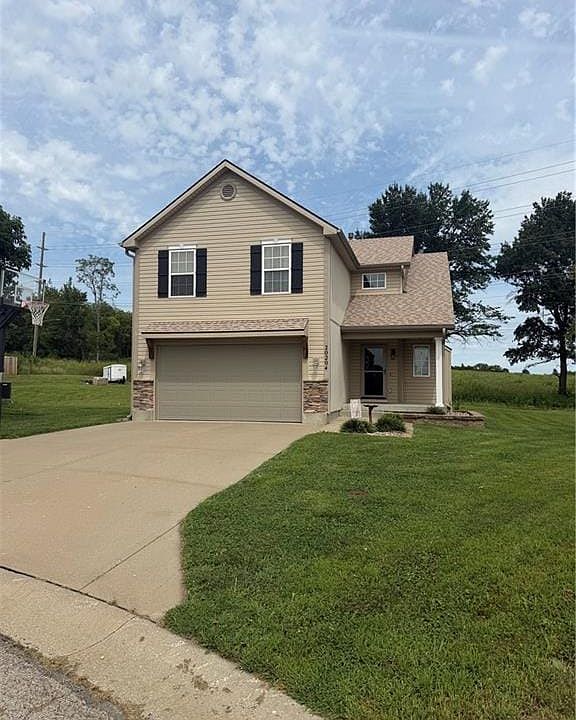 Two-story residence featuring light-colored siding, dark shutters, an attached garage, a concrete driveway, and a front porch
