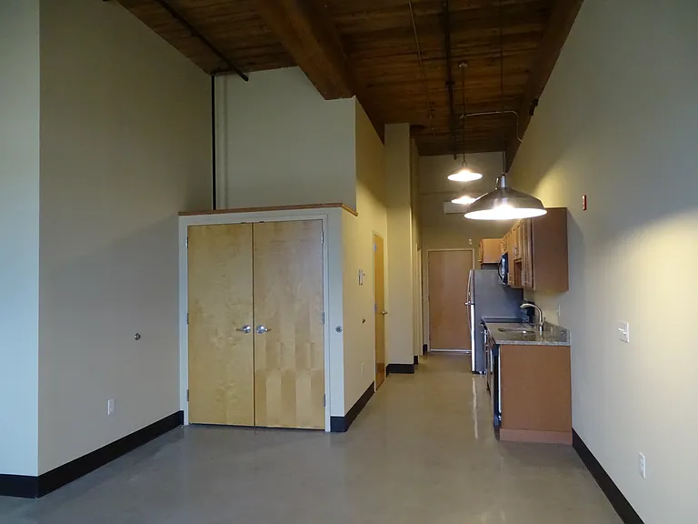Studio, view from living area to kitchen, with closet, bathroom and storage area.