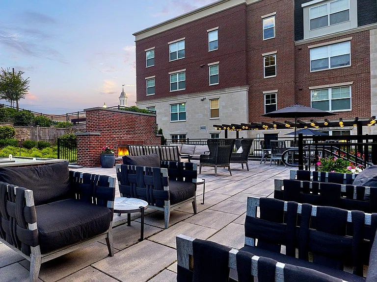 Elegant outdoor patio space with modern seating, cozy fire pit, and ambient lighting against a charming brick building backdrop.