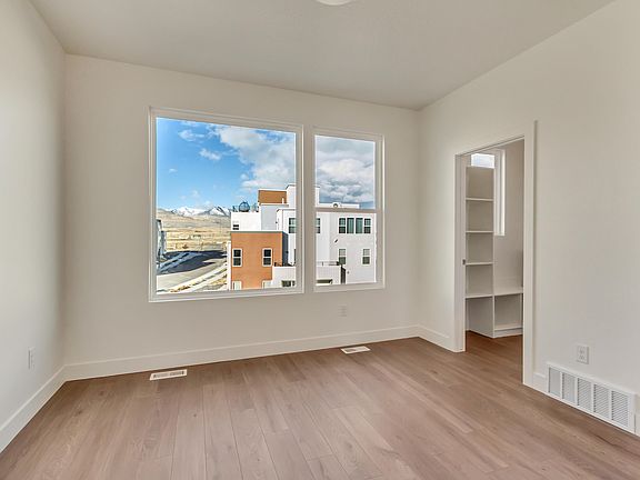Bright room with wooden floor, large windows showing an urban view and hills, and an open doorway to