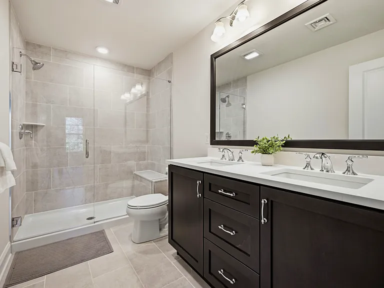 Bathroom in the primary bedroom has a dual sink vanity with quartz counter and beautiful frameless shower with a deep bench.