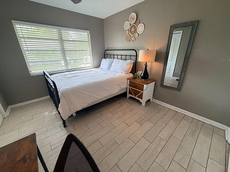 Well-sized bedroom with a large window, tile flooring, and space for a bed, nightstand, and a small work area.