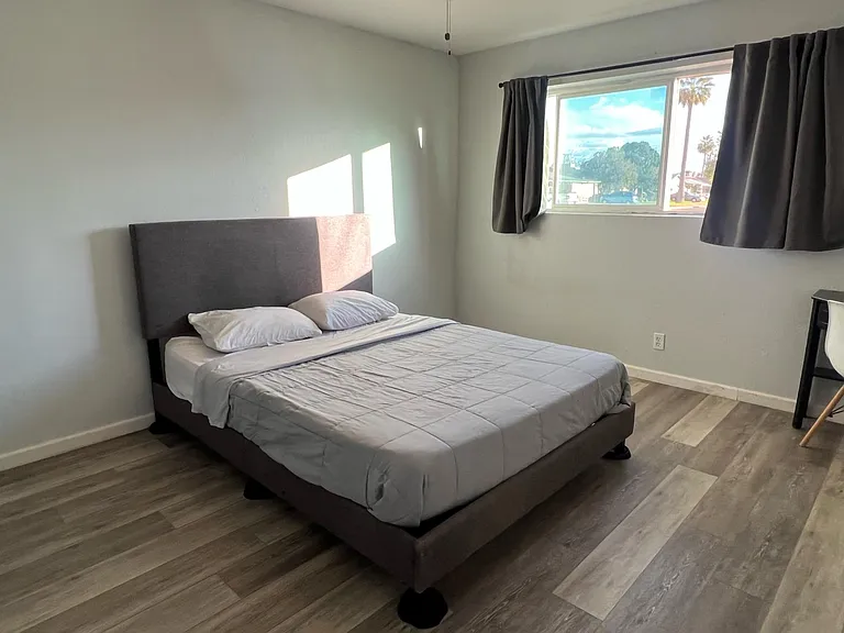 Private bedroom with a comfortable bed, durable flooring, and a large window with curtains for light and privacy.