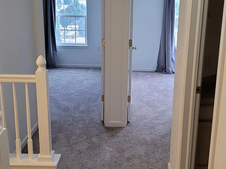 View from master bedroom door to hallway leading to full bathroom, stairs, and two smaller bedrooms.