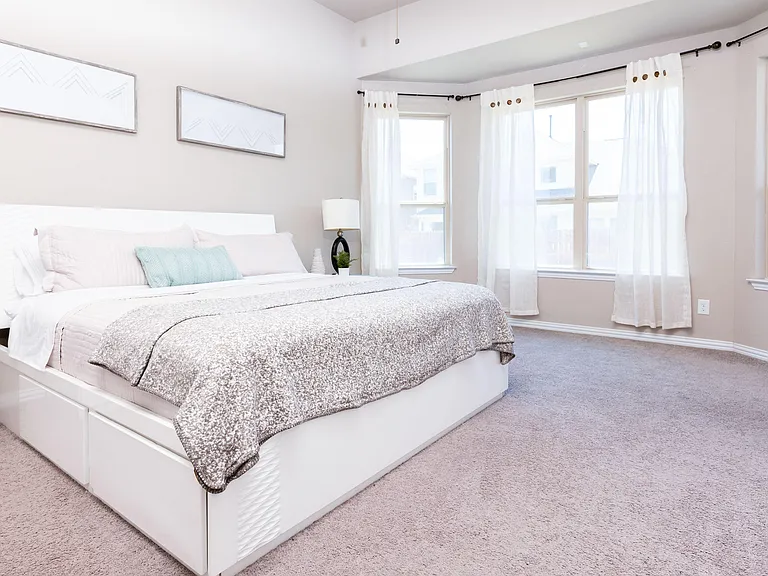 Spacious bedroom featuring a large bed, plush carpet, and wide windows with curtains for ample natural light.
