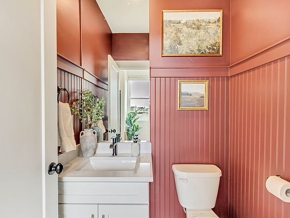 A bathroom with reddish-brown paneled walls, a white sink and vanity, a white toilet, a towel ring w