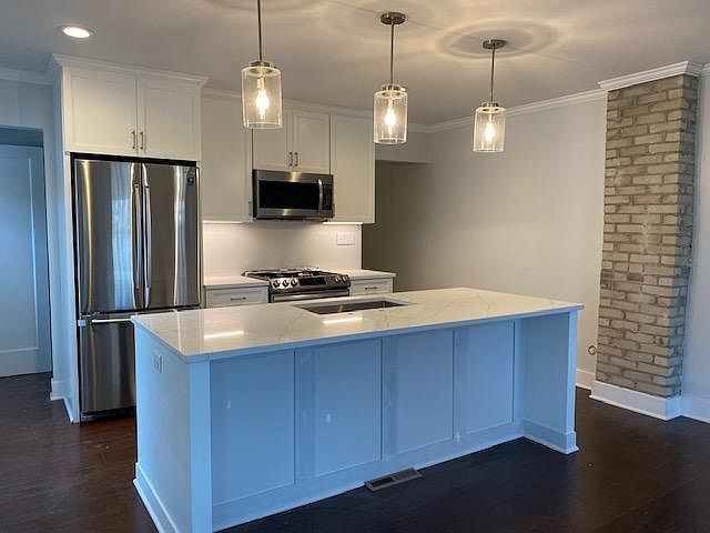 Fully renovated kitchen with new, stainless steel appliances including dishwasher, large quartz island that seats four, and brand new lighting. The exposed brick may be left as is or painted white.