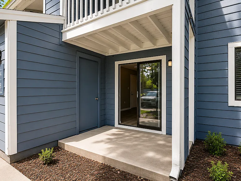 Inviting apartment entrance with modern blue siding and spacious front patio, promising a warm welcome.