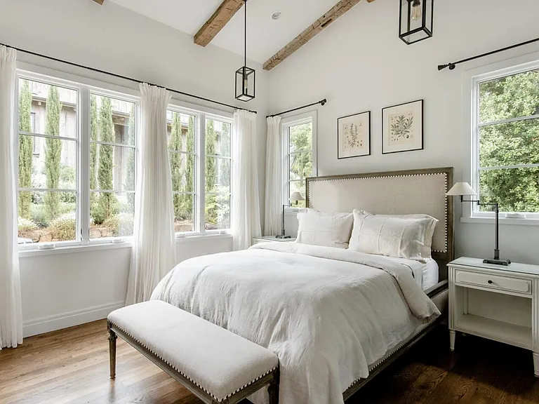 large windows surrounding the bedroom with both sheer and semi-solid curtains