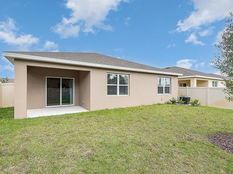 Charming backyard view of a modern single-story home with a spacious lawn, a covered patio, and a perfect mix of privacy and comfort.