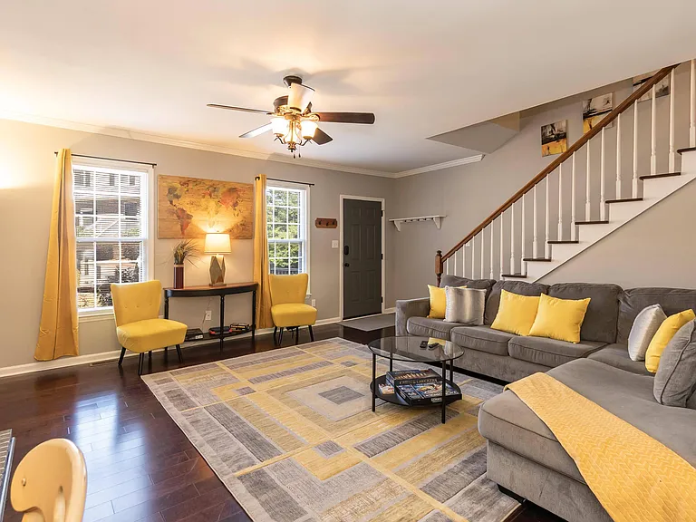 Spacious living room with sectional seating, ceiling fan, and large windows, plus convenient entryway and staircase access.