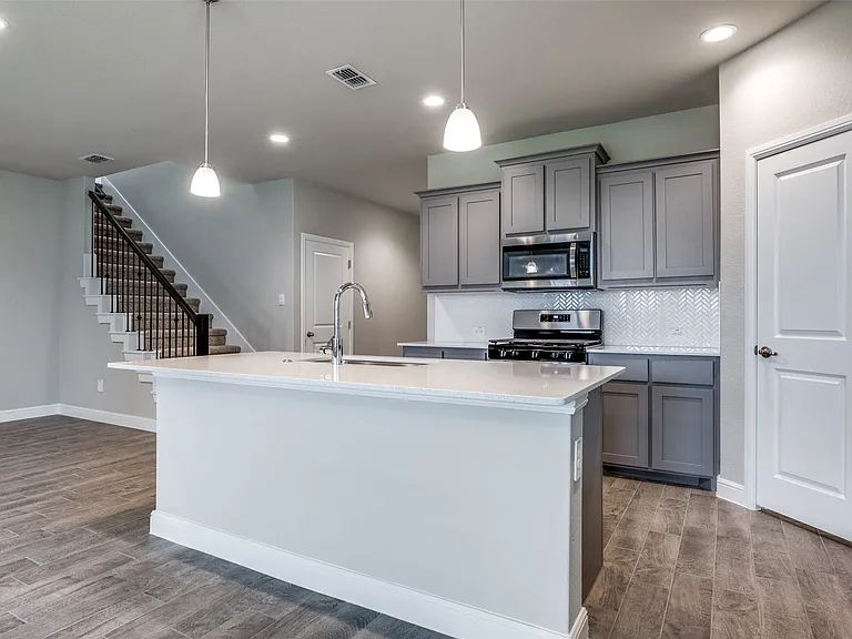 Kitchen featuring decorative light fixtures, stainless steel appliances, an island with sink, wood-type flooring, and sink