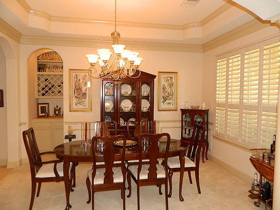  Formal dining room has a dry bar with wine storage, tray ceilings and crown moldings and plantation shutters with views of the front gardens.