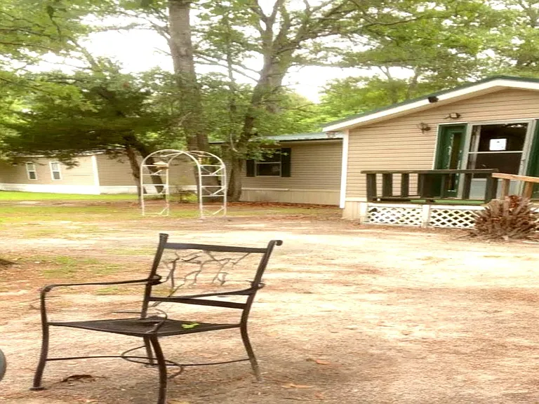 Shaded yard with a ramped porch entry and outdoor space for relaxing or entertaining under mature trees.