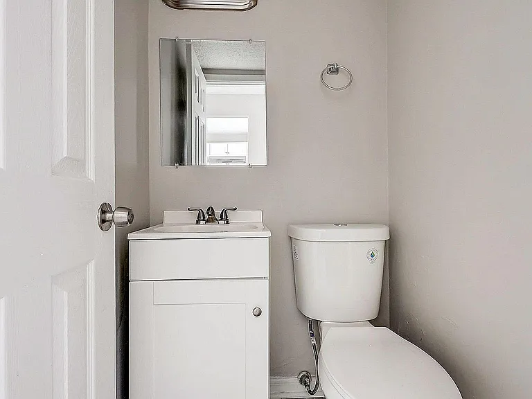 Modern bathroom with sleek fixtures, featuring a compact white vanity, a wall-mounted mirror, and a pristine toilet set against neutral walls.