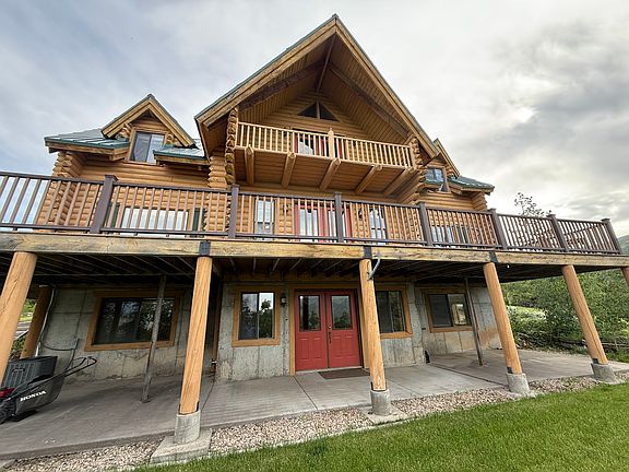 View of cabin at ground level from the north, showing the basement walkout, main floor deck, and top floor north balcony.