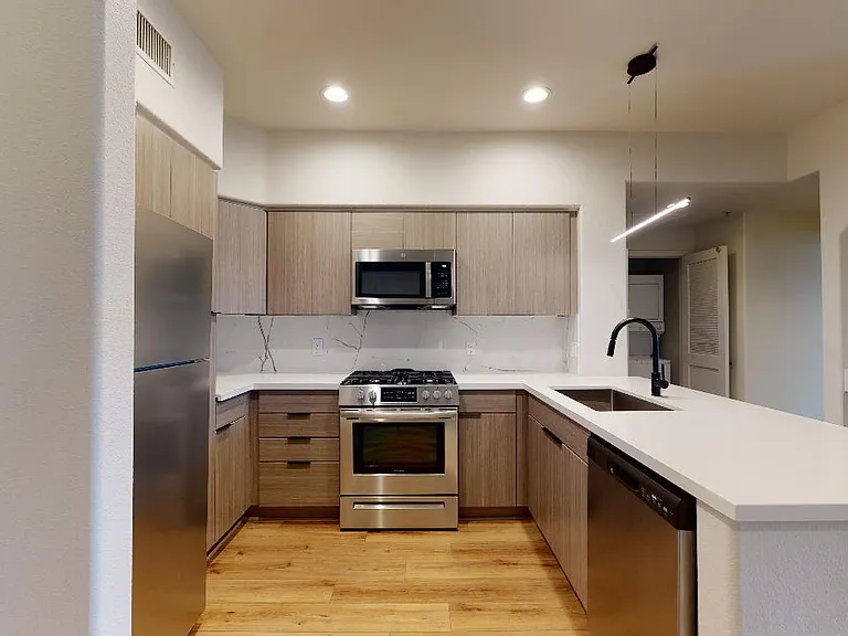 Apartment kitchen with stainless steel appliances, quartz countertops, and wood-style flooring.