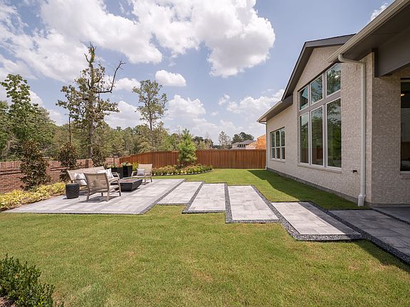 A well-manicured backyard with a paved patio, lush green lawn, and a modern house with large windows