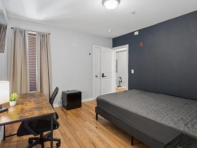 Private furnished bedroom with hardwood floors, window treatments, and a dedicated desk area for work or study.