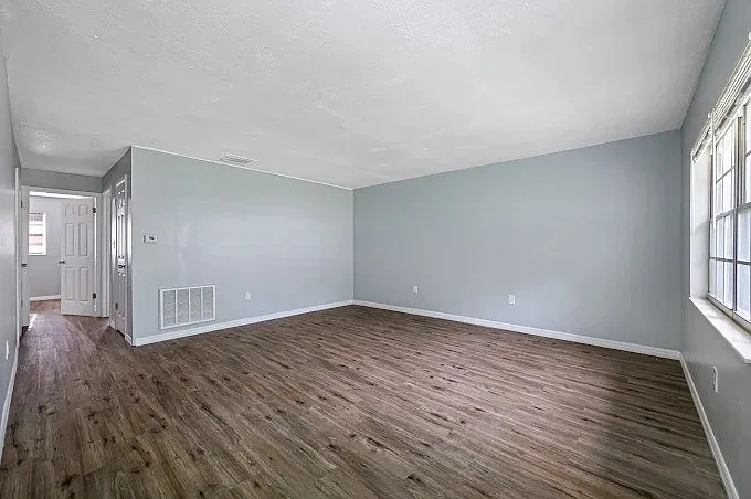 Bright and inviting living area with elegant wooden flooring and large window, perfect for a cozy home atmosphere.