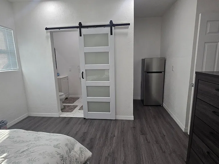 Spacious bedroom with durable plank flooring, a large window, and direct access to an adjacent bath via a sliding barn door.