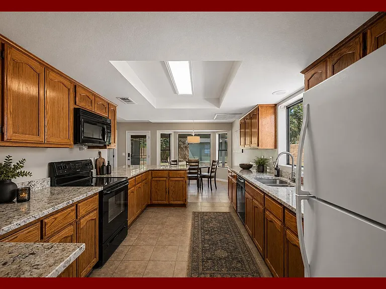 Spacious galley kitchen with ample wood cabinetry, granite counters, and a full appliance suite, opening to the dining area.