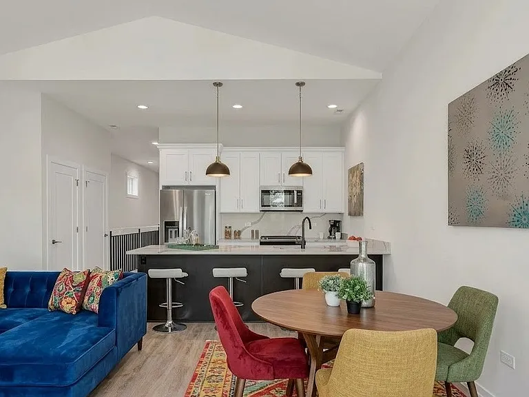 Living Room (Angle 2): Dining area with round walnut table, velvet chairs, and a blue sofa