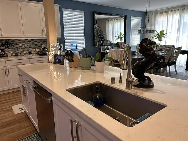 Open kitchen with a large quartz island, undermount sink, and ample white cabinetry, flowing into the dining area.