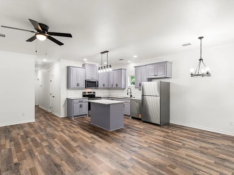 Kitchen featuring stainless steel appliances, light gray cabinetry with dark hardware, white subway tile backsplash, and an island with a light-colored countertop