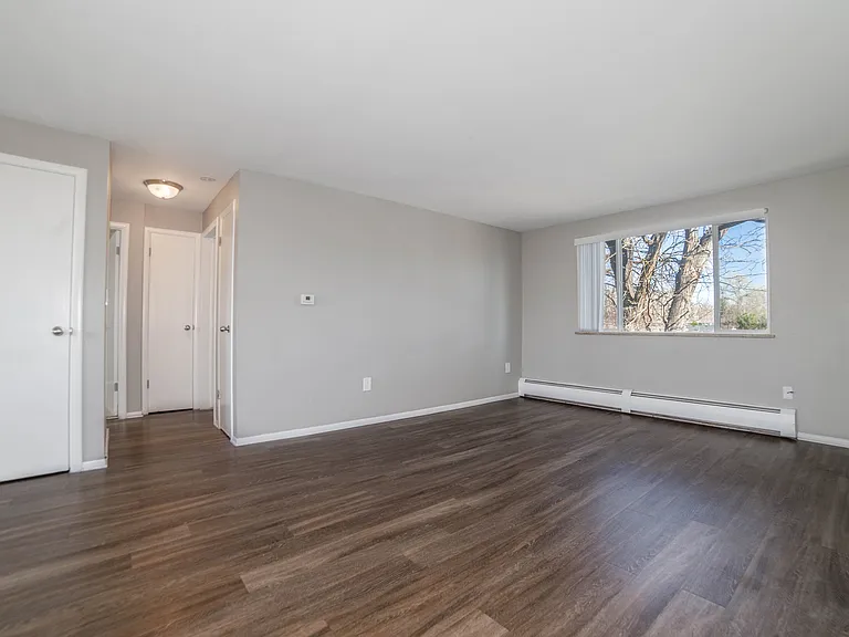 Spacious modern living room with sleek hardwood floors and large window providing plenty of natural light.