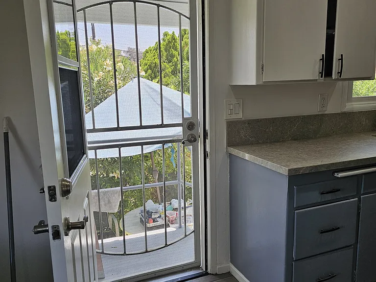 Rear door, with kitchen to the right. Outside of rear door is stair landing, leading down to outside table, chairs and umbrella.