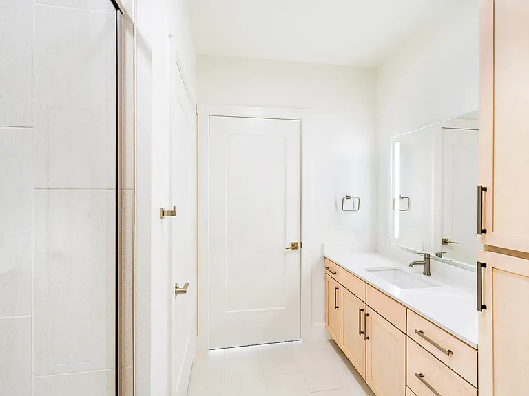 Primary bathroom with a double vanity, light wood cabinetry, integrated lighting, and a glass-enclosed shower arranged for daily routines.