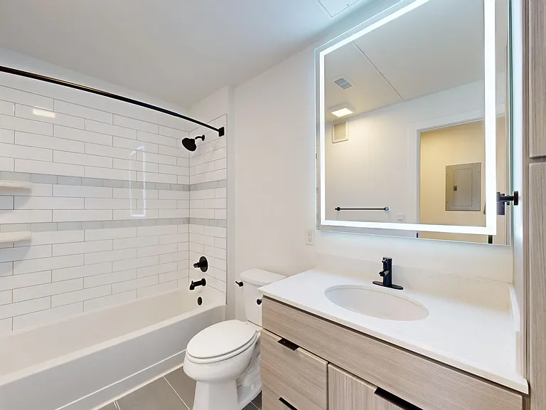 Apartment bathroom with wood-style flooring and LED vanity mirror.