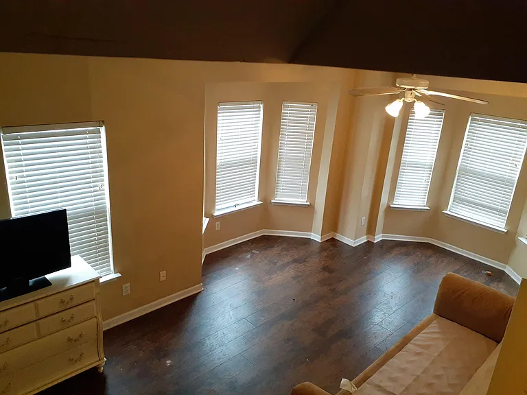 Spacious living area with bay-style windows, ceiling fan lighting, and durable wood-look flooring for easy upkeep.